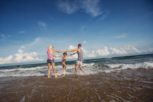 Happy young family having fun running on beautiful beach with waves and sea foam. Family traveling concept