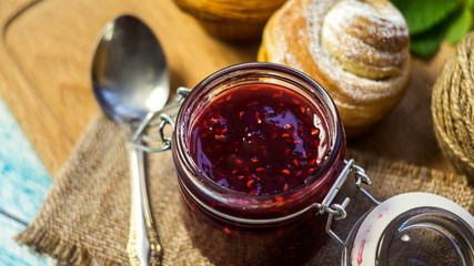 raspberry jam in a jar and muffins. selective focus, top view