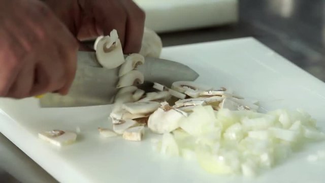 Chef hand cutting with knife champignon mushrooms 4k close up video. Food preparing in restaurant kitchen