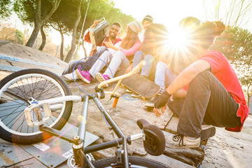 Group of trendy friends having fun together out at skate bmx park - Youth friendship concept with young people outdoors - Focus on afroamerican with stereo - Retro vibrant filter with sunflare halos