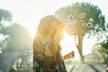 Young afro hair woman blowing soap bubble in city skate park