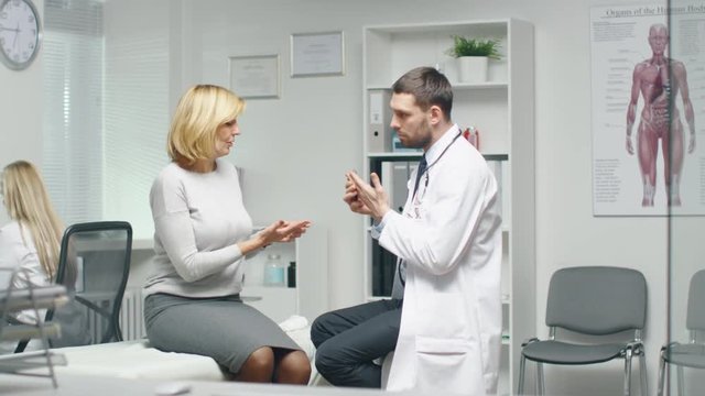 Young Male Doctor Consults His Mid Adult Female Patient. They are Checking Her Hands. Shot on RED Cinema Camera in 4K (UHD).