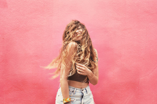 Fun and colorful. Young pretty happy woman with long wavy hair on her face posing and smiling against pink wall