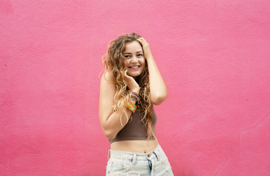 Fun and colorful. Young pretty happy woman with long wavy hair posing and smiling against pink wall