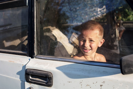 Little boy looking and squinting through window glass playing in old rusty car outdoor