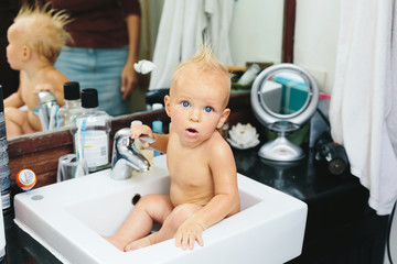 Little funny baby child with funny hairstyle sitting in sink after bath hygiene