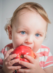 The child holds and eats an apple