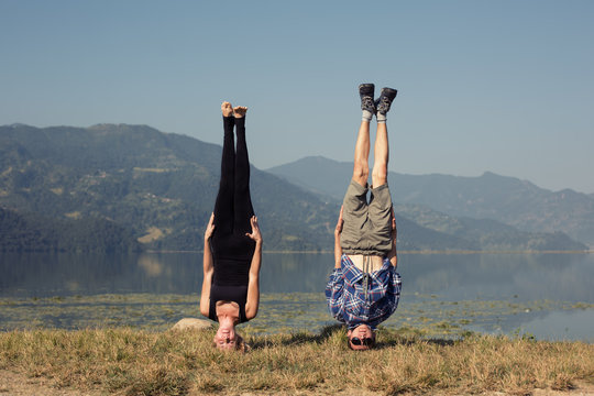 Couple of young yogis stand on his head while doing yoga headstand asana. Beautiful mountain lake landscape background. Complex amazing yoga picture