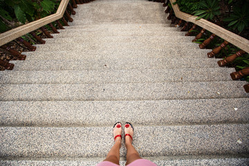 Female feet in sandals on the top of big steps down. Long pathway downstairs