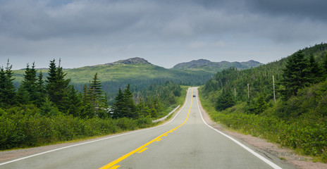 Newfoundland highway in overcast skies.  Lone car goes down the road.  Coastal highways in foothills and valley ranges of Newfoundland.  - 129012466