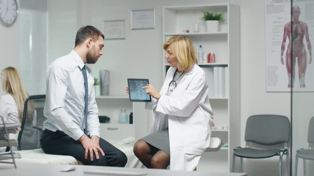 Mid Adult Female Doctor Consults Young Man Mid Adult Female Doctor Consults Young Man About His Back Pain. Doctor Shows Him Tablet Computer With His Spine X-Ray. Shot on RED Cinema Camera in 4K (UHD).