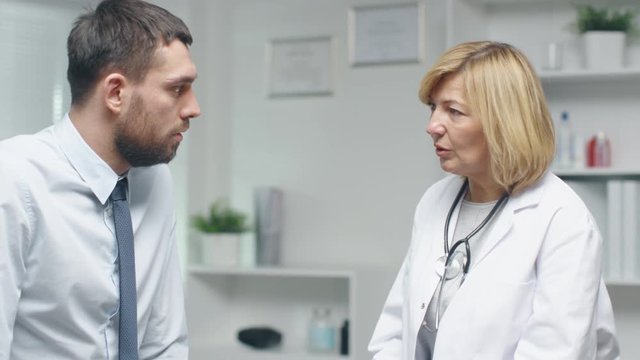 Mid Adult Female Doctor Talks Seriously with Her Male Patient. Shot on RED Cinema Camera in 4K (UHD).