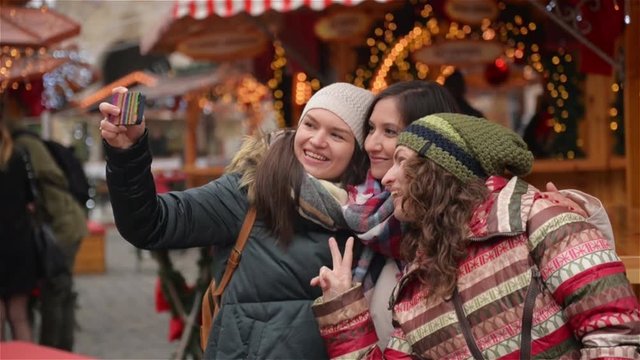 Three Girlfriends Taking a Selfie with Smart Phone on the Christmas Market. Happy Women Having Fun Outdoors on the Xmas Fair. Merry Christmas and Happy New Year