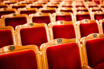 Sets on an empty theatre, taken with selective focus and shallow depth of field. Empty vintage red seats with numbers, teather chair, cinema seats. Movie theater auditorium with lines of red chairs. - obrazy, fototapety, plakaty