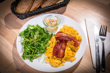 Breakfast table with crambled eggs, bacon and ruccola salad on the plate