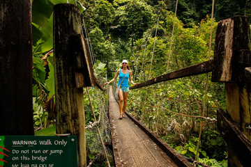 Young woman walking on suspension bridge over Wainibau stream, L - obrazy, fototapety, plakaty