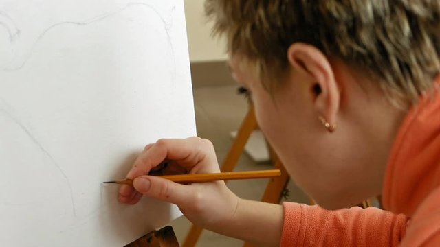 Female artist draws a pencil sketch drawing on canvas easel in art studio. Student girl learning to draw and paint.