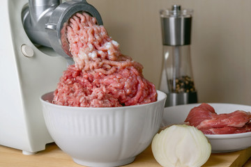 Cooking food. On wooden table electric grinder and a bowl of meat. On the table was the onion and mill. Raw minced pork and onions.