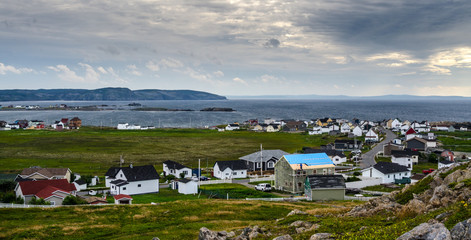 Fototapeta na wymiar Bonavista, Newfoundland, Canada, mid summer, overcast day. Seaside village community. People staying inside on blustery day except one man working on his roof.