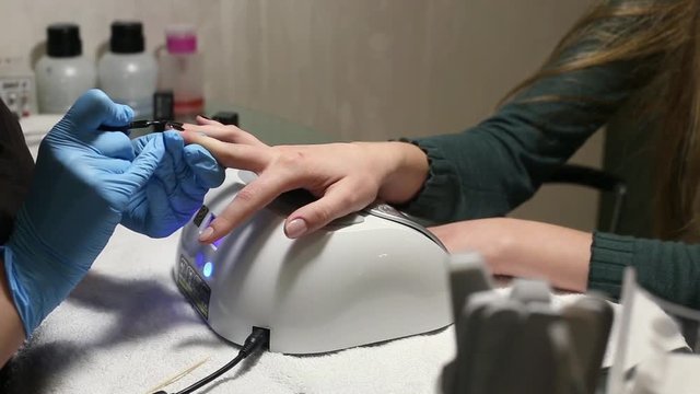 manicurist makes the manicure for young caucasian woman in beauty salon. hands close up