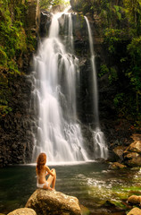 Fototapeta na wymiar Young woman in bikini sitting by Middle Tavoro Waterfalls in Bou