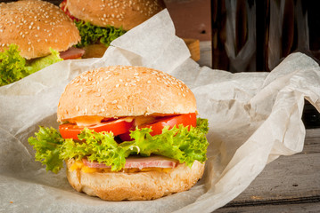 Freshly prepared homemade burgers: a bun with sesame seeds, meat, cheese, lettuce, tomato and cheese sauce, copy space