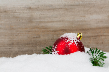 Red christmas ball with green branch in snow on wooden backgroun