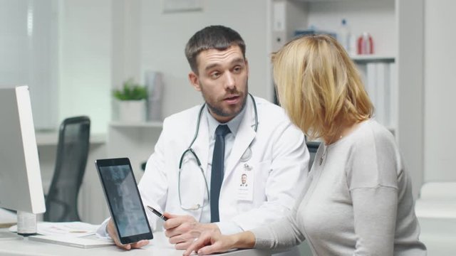 Professional Doctor Consults Mid Adult Woman. He Points out Something on the Screen to Her. They Both Laugh.  Shot on RED Cinema Camera in 4K (UHD).