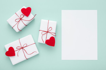 Valentine day composition: white gift boxes and red bows and red felt hearts with white card for text, photo template, pastel blue background. Top View. View from above.