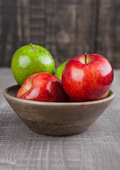 Red and green apples in wooden bowl on board