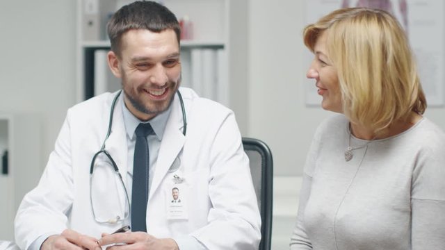 Male Doctor Consults Mid Adult Female Patient. They Talk and Smile.  Shot on RED Cinema Camera in 4K (UHD).