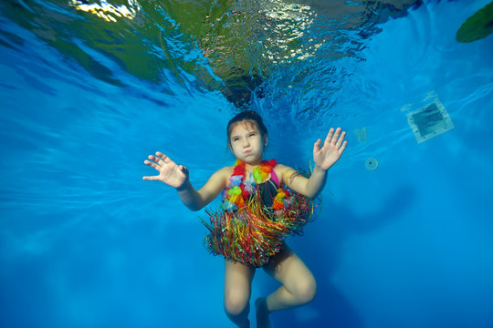 Happy little girl swimming and dancing underwater in the pool in costume for carnival on a blue background. Shooting under water. Portrait. Horizontal orientation