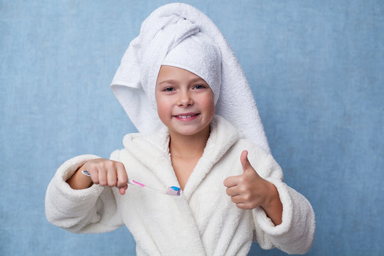 Little smiling girl holding a toothbrush in the hand and showing thumb up gesture, blue background