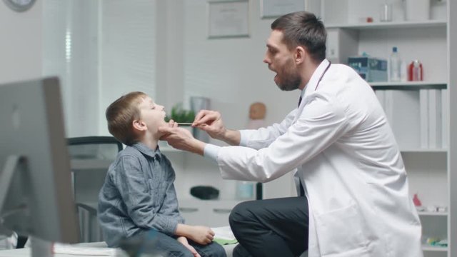 Male Doctor Checks Young Boys Throat. Nurse is Busy in the Background. Shot on RED Cinema Camera in 4K (UHD).