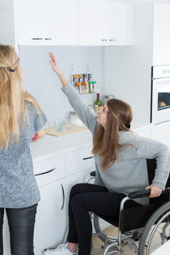 Disabled Young Woman In Wheelchair For Reaching Dishes From Cupboard