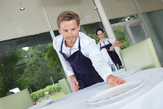handsome happy waiter setting up a table at restaurant