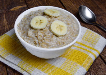 oatmeal in a beautiful white bowl on a warm wooden background with slices of bananas