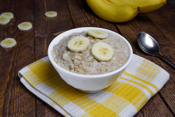 oatmeal in a beautiful white bowl on a warm wooden background with slices of bananas