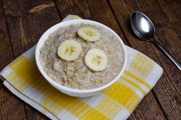 oatmeal in a beautiful white bowl on a warm wooden background with slices of bananas