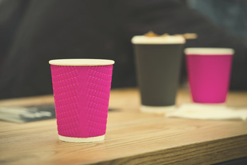Black and pink craft paper coffee cups in cafe on wooden table. Lifestyle, coffeeshop concept.