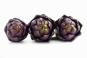 Fototapeta premium three purple artichokes from italy in a row, front shot, isolated on white