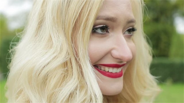 A blond young girl with a red lipstick smiling. Slow motion.