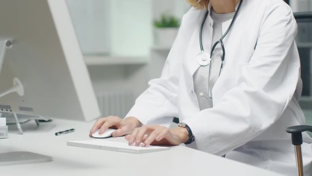 In the Doctor's Office. Mid Adult Female Doctor Works at Her Desktop Computer. In the Background Her Assistent's Works at His Desk.
 Shot on RED Cinema Camera in 4K (UHD).