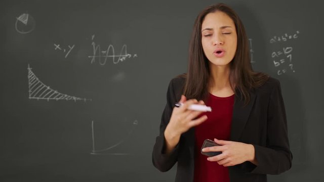A Hispanic woman teacher explains math to students on a chalk board