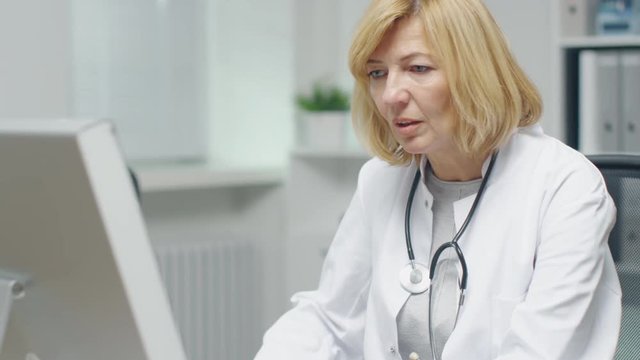In the Doctor's Office. Mid Adult Female Doctor Works at Her Desktop Computer. In the Background Her Assistent's Works at His Desk.
 Shot on RED Cinema Camera in 4K (UHD).