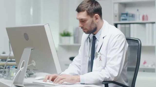  Close-up of a Male Doctor is Working at His Desk. He Uses Personal Computer and Consults Documents. Shot on RED Cinema Camera in 4K (UHD).