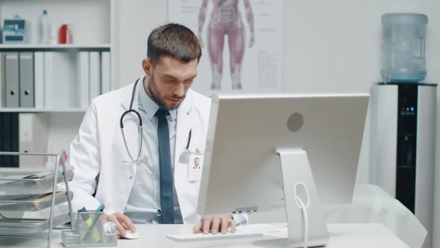 Close-up of a Male Doctor is Working at His Desk. He Uses Personal Computer and Consults Documents. Shot on RED Cinema Camera in 4K (UHD).