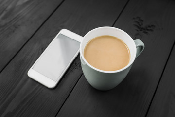 Cup of coffee and smart phone with white screen on the black wooden background.