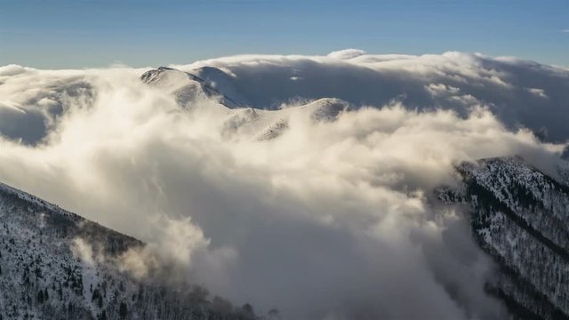 Winter snowy mountains with low clouds flying over ridge in morning light time lapse