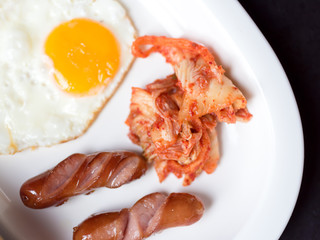 fried egg sausage and Kimchi  serve as  breakfast  in white dish 